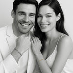 Couple wearing matching Morse code bracelets — woman in 18k gold and man in oxidized silver, minimal black-and-white editorial portrait by 143Code