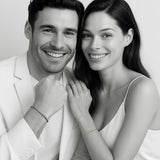 Couple wearing matching Morse code bracelets — woman in 18k gold and man in oxidized silver, minimal black-and-white editorial portrait by 143Code
