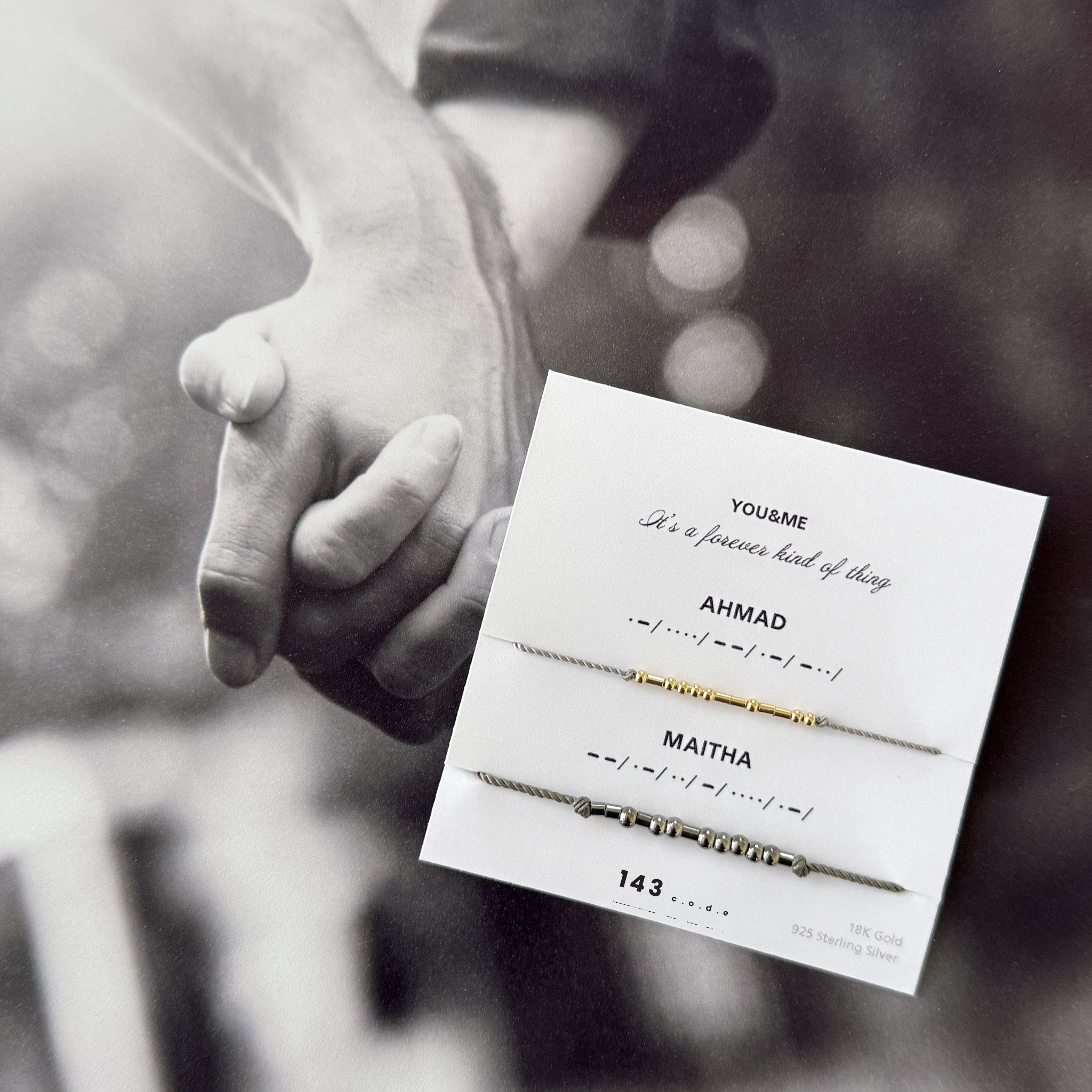 Matching Morse code couple bracelets on personalized card — 18k gold and oxidized silver set, styled on black-and-white photo of holding hands